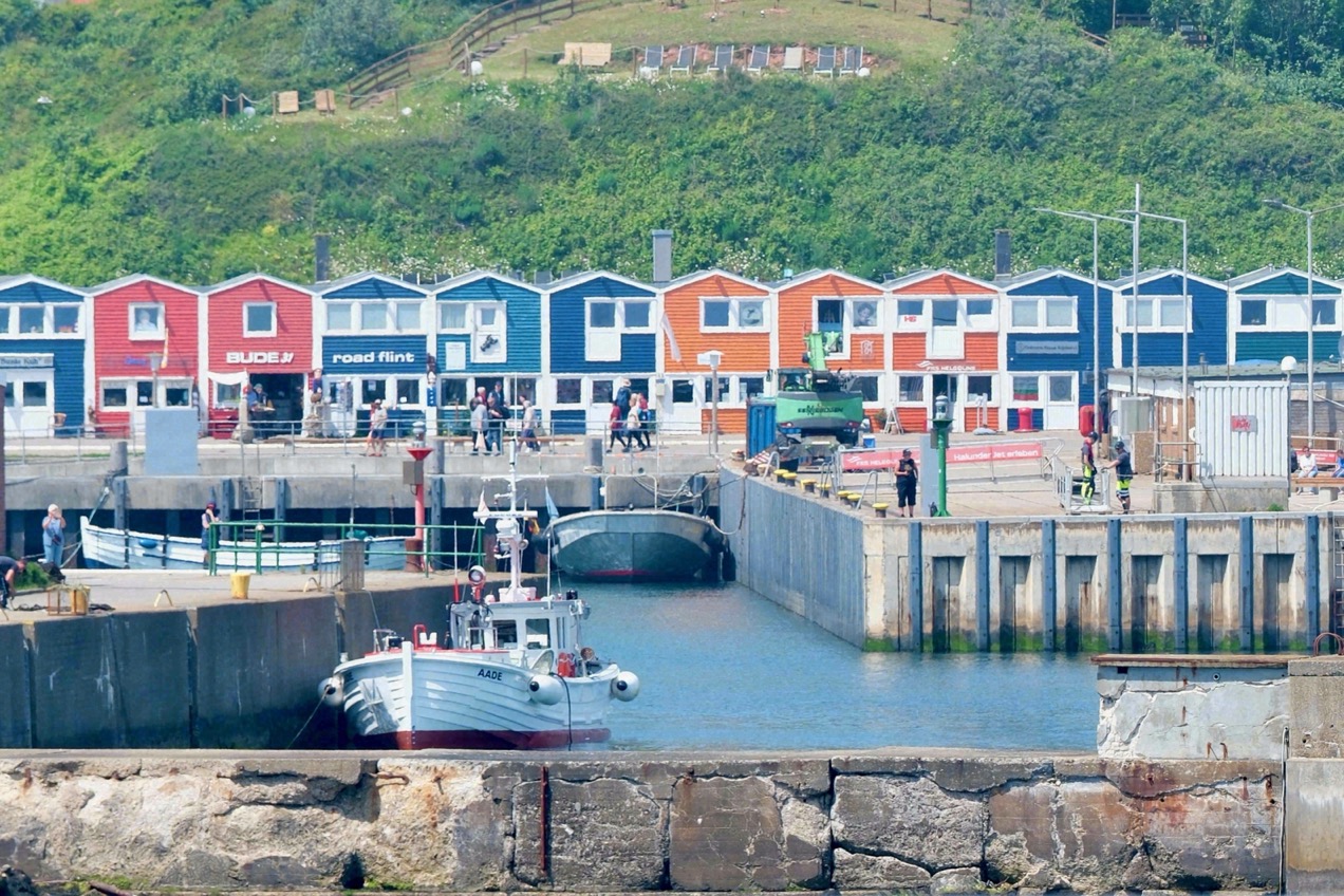Die bunten Hummerbuden am Helgoländer Hafen, davor kleine Fischerboote am Kai.